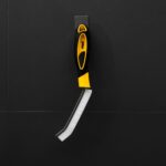 Szczotka do czyszczenia fug zawieszona na czarnej ścianie, z ergonomicznym, żółto-czarnym uchwytem.