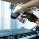 Czyszczenie lusterka w samochodzie ściereczką przez osobę w czarnych rękawiczkach.