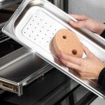 Czyszczenie stalowej tacy piekarnika przy użyciu gąbki, widok zbliżeniowy.