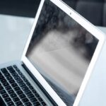 Zamknięty biały laptop na biurku, odbijający rozmyty obraz na ekranie.