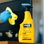 Żółta butelka środka do czyszczenia ekranów LCD, w tle ekran czyszczony szmatką.