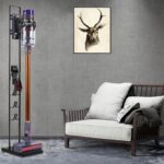 Bezprzewodowy odkurzacz w nowoczesnym salonie z szarą kanapą i obrazem jelenia na ścianie.