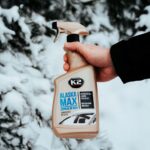 Odmrażacz do szyb K2 Alaska Max w ręku, tło z zimowym krajobrazem. Idealny na zimowe poranki.