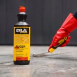 Butelka płynu do czyszczenia fug ERLA Fuger, obok osoba z czerwoną rękawicą trzyma szczotkę. Idealne do fug i spoin.