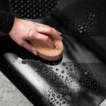 Ręka czyszcząca czarną powierzchnię z wodą i bąbelkami przy użyciu gąbki.