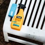 Żółty środek czyszczący na plastikowe meble i niebieska ściereczka na białym plastikowym krześle w ogrodzie.