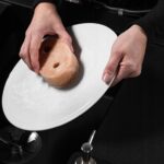 Osoba myje biały talerz gąbką w zlewie, przedstawiając proces ręcznego mycia naczyń.