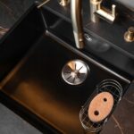 Czarny zlew kuchenny ze złotą baterią, metalową kratką i gąbką, stylowy design wnętrza.