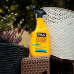 Żółty płyn czyszczący Erla Kliv do mebli ogrodowych, na tle doniczek z roślinami i krzewów.