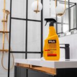 Butelka środka czyszczącego Saniz Shine na umywalce w nowoczesnej łazience z eleganckim złotym prysznicem i lustrami.