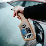 Osoba używa odmrażacza do szyb K2 Alaska Max na oszronionej szybie samochodowej, aby szybko usunąć lód.