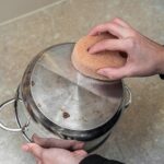 Ręczne mycie garnka ze stali nierdzewnej gąbką na zabrudzenia i przypalone resztki.