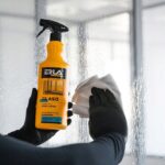 Płyn do mycia szyb i luster ERLA w żółtej butelce, używany do czyszczenia powierzchni szklanych ręcznikiem.