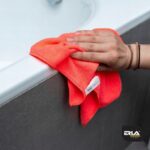 Ręka czyszcząca wannę pomarańczową ściereczką z mikrofibry marki Erla Home. Idealna do sprzątania łazienki.