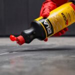 Ręka w czerwonej rękawicy wlewa płyn z butelki na podłogę, preparat do fugowania ERA FUGER.