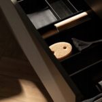 Otwarta szuflada z organizerem, zawierająca różne akcesoria kuchenne na drewnianej podłodze.