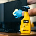 Czyszczenie ekranu komputera płynem ERLA. Idealny do monitorów LCD. Ręka w rękawiczce poleruje powierzchnię.