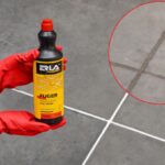 Osoba trzyma płyn do czyszczenia fug ERLA na tle płytek podłogowych.