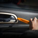 Osoba używa narzędzia do demontażu panelu drzwi samochodu, ukazując wnętrze i uchwyt drzwi.