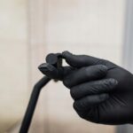 Ręka w czarnej rękawiczce trzyma mały czarny przedmiot, prawdopodobnie część wyposażenia technicznego lub narzędzia.
