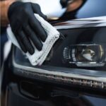 Ręczne polerowanie reflektora samochodowego czystą szmatką przez osobę w rękawiczkach ochronnych.