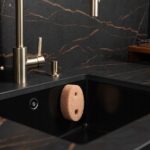 Gąbka do naczyń w czarnym zlewie kuchennym, marmurowy blat i stylowa armatura.