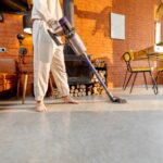 Osoba odkurzająca jasną podłogę w nowoczesnym wnętrzu z czerwonej cegły; domowe porządki.