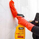 Osoba w rękawicach sprząta płytki, używając środka czyszczącego Saniz Shine od marki Erla.